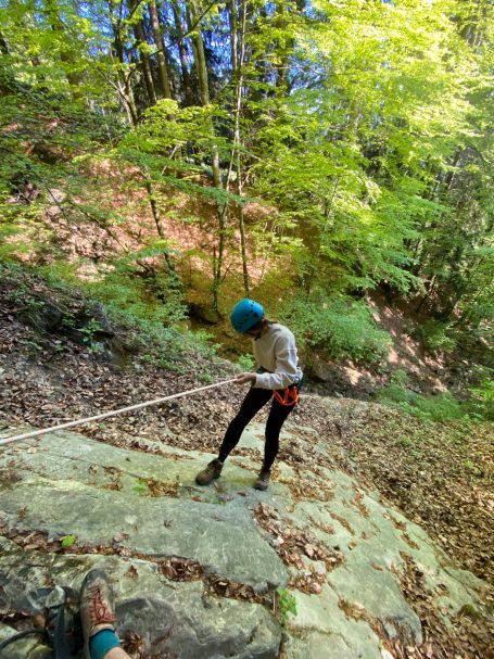 Zipline Allgäu abseilstelle Person sichert sich beim Klettern an einer Felswand in bewaldeter Umgebung.
