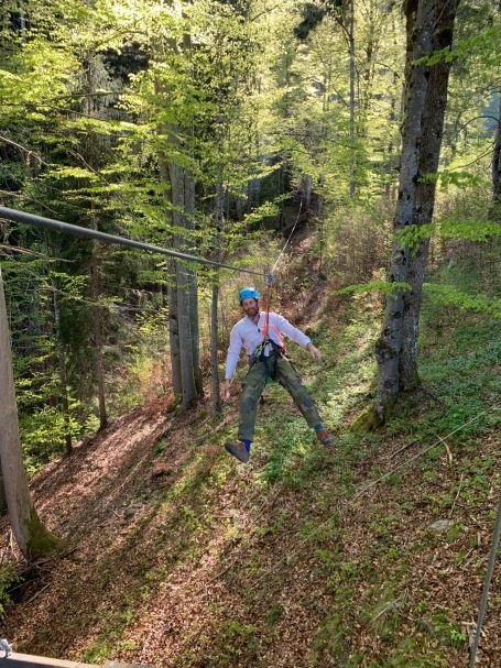 Landeanflug Zipline Allgäu Person rutscht an einer Zipline im Klettergurt umgeben von bäumen im Allgäu entlang